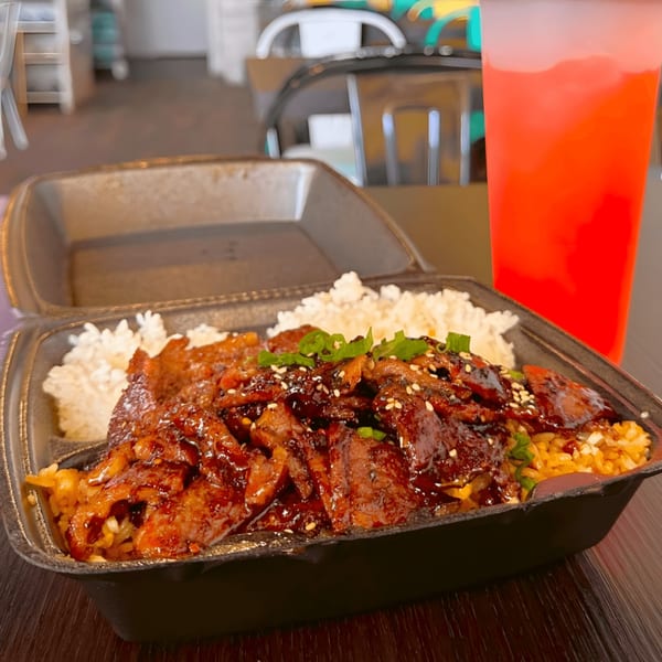 Teriyaki chicken with white rice and yellow rice, garnished with green onions and sesame seeds, next to a red drink.