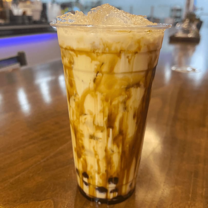 A tall plastic cup of Sharky's Island Bites' brown sugar boba milk tea with ice.