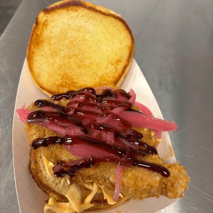 Crispy chicken sandwich with pickled red onions and dark sauce on a toasted bun.