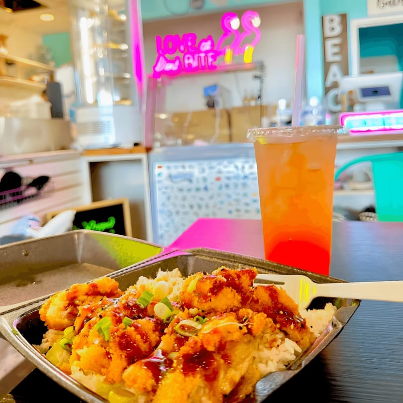 Sharky's Island Bites poke bowl with crispy chicken, rice, and green onions, next to a colorful drink.